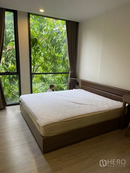 Condominium for rent in Watthana, Bangkok - Master bedroom with king bed and corner floor-to-ceiling windows with greenery views.