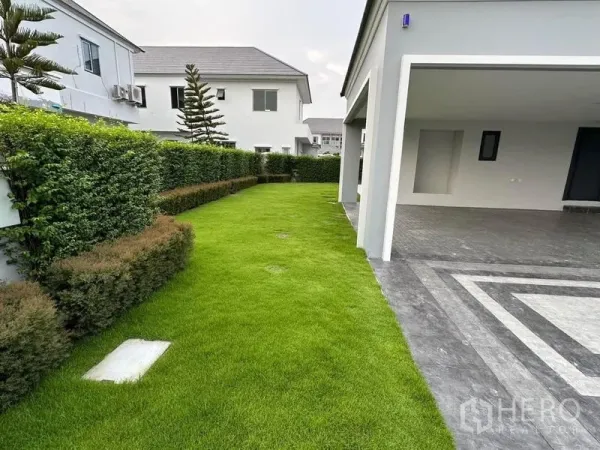 บ้าน ขายในLat Krabang, Bangkok - สนามหญ้าด้านข้างติดที่จอดรถมีหลังคาและทางเข้าเทา