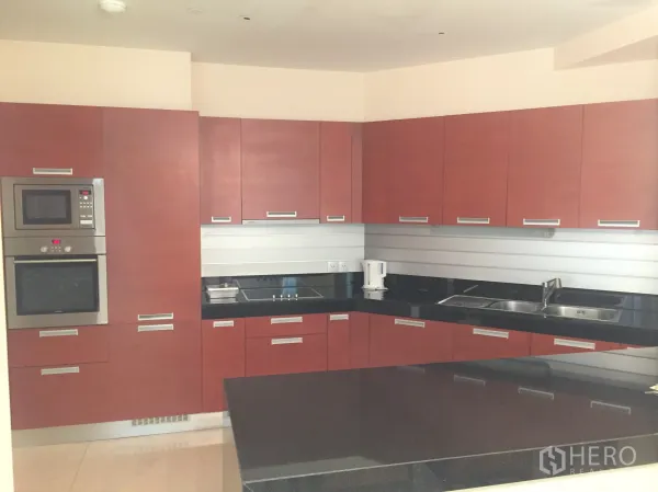 Condominium for rent in Bang Rak, Bangkok - Modern kitchen with red cabinetry, black granite counters, built-in oven and microwave.