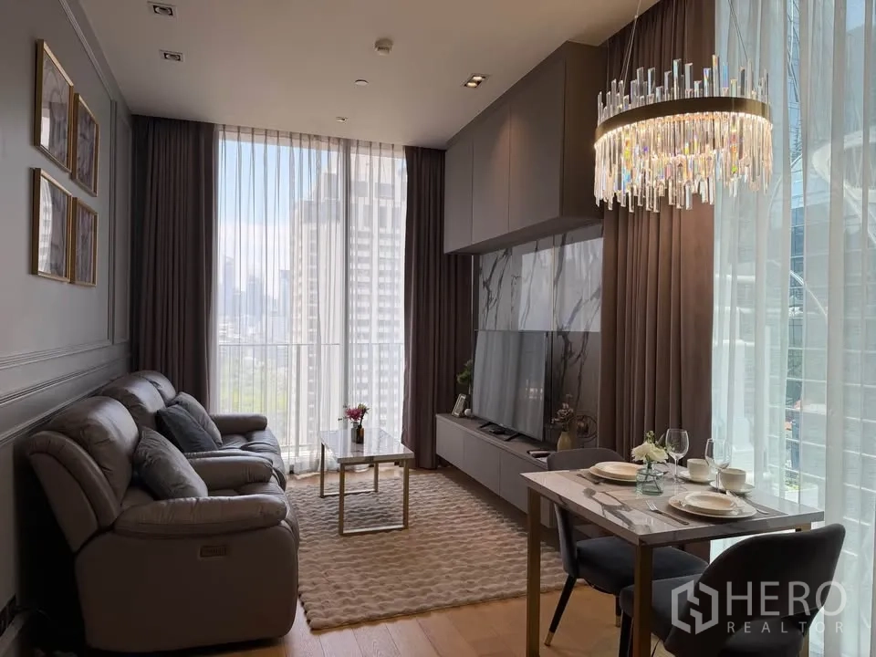 คอนโด for rent in Pathum Wan, Bangkok - ห้องนั่งเล่นและรับประทานอาหารสว่างด้วยกระจกสูงจรดเพดาน เห็นวิวเมืองและสวน พร้อมโซฟา ผนังทีวี และโคมไฟแชนเดอเลียร์