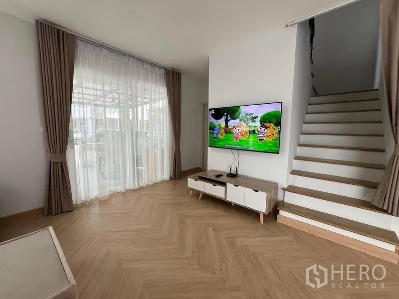 Detached House for rent in Bang Phli, Samut Prakan - Living room with herringbone floors, TV wall, staircase, and floor-to-ceiling curtains.