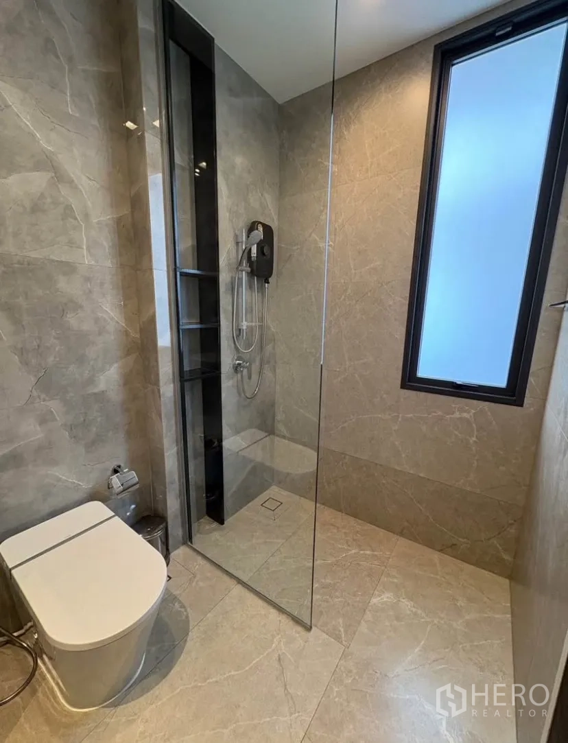 Detached House for rent in Suan Luang, Bangkok - Modern bathroom with glass-enclosed shower, gray marble tiles and a window.