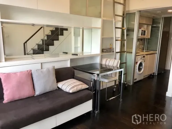 公寓 出租在Khlong Toei, Bangkok - 开放式客厅，沙发与餐桌，旁接厨房与置物架。