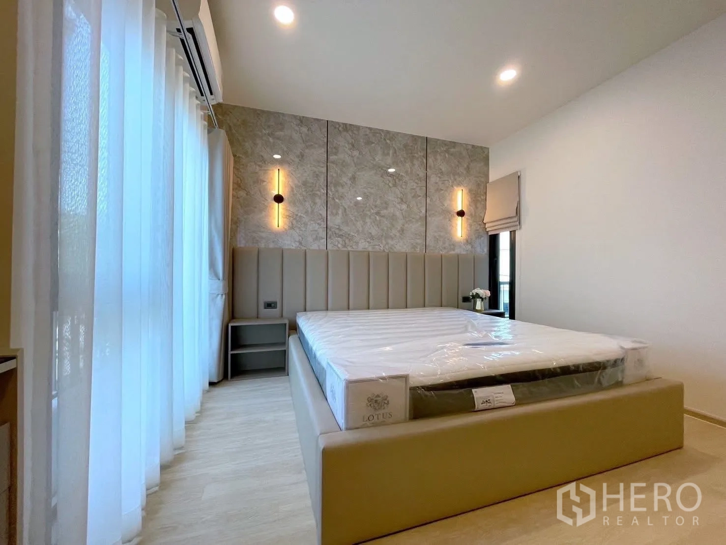Detached House for rent in Bang Phli, Samut Prakan - Elegant bedroom with marble accent wall panels, warm sconces, upholstered bed and sheer curtains.