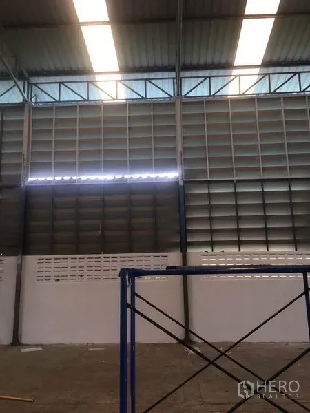 Warehouse for rent in Samut Prakan - Warehouse interior with high steel-truss roof, skylights and ventilated louvered side panels above a solid block wall.