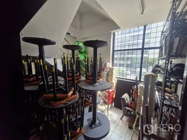 Shophouse for rent in Pathum Wan, Bangkok - Storage room with stacked bar stools under stairs and a large grid window.