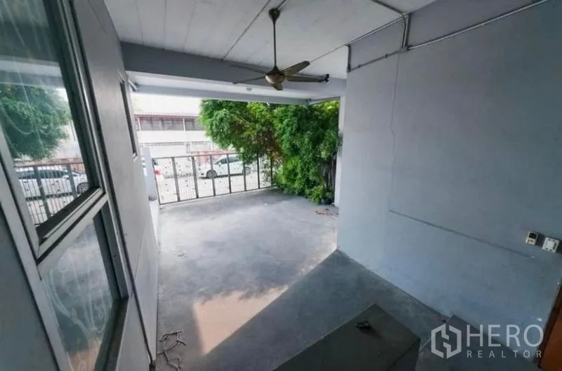 สำนักงานที่บ้าน ให้เช่าหรือขาย - เฉลียงครอบคลุมพร้อมพัดลมเพดาน มองออกไปยังด้านหน้าที่มีกำแพงรั้วและต้นไม้ใหญ่