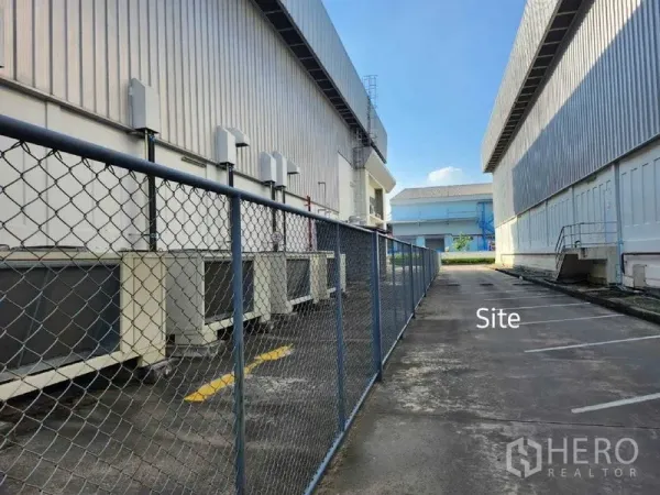 Warehouse for rent in Bang Phli, Samut Prakan - Service lane between warehouse buildings with chain-link fence and exterior HVAC units.