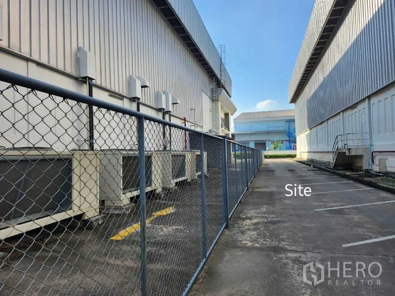 Warehouse for rent in Bang Phli, Samut Prakan - Service lane between warehouse buildings with chain-link fence and exterior HVAC units.