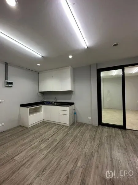 พื้นที่ขายปลีก ให้เช่าในKhlong Toei, Bangkok - มุมครัวขนาดกะทัดรัด ตู้สีขาว เคาน์เตอร์สีดำ พื้นลายไม้ และประตูกระจกบานเลื่อน