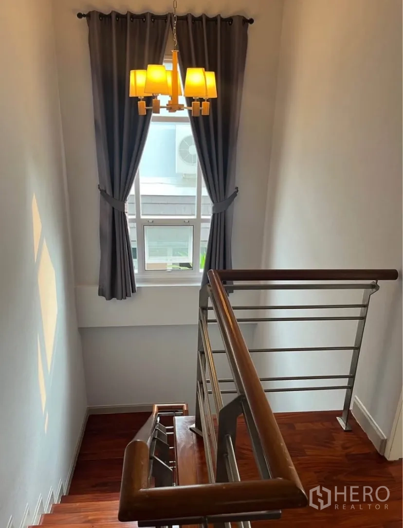 独立式住宅 出租或出售在Lat Phrao, Bangkok - 楼梯间带木阶与不锈钢扶手，吊灯和窗帘窗户。