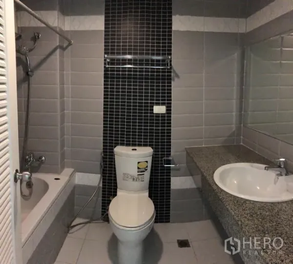 公寓 出租在Watthana, Bangkok - 浴室配浴缸与花洒、黑色装饰墙砖、坐便器及宽大石材台盆。