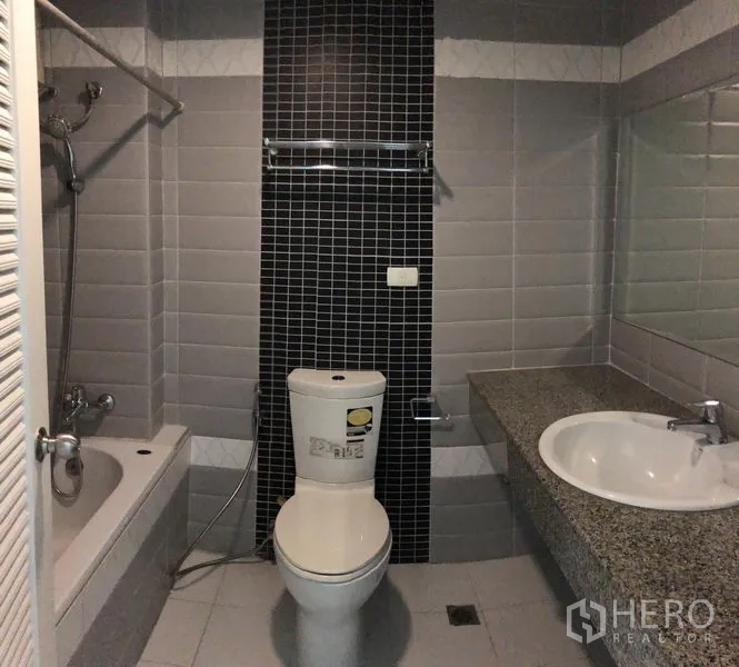 公寓 出租在Watthana, Bangkok - 浴室配浴缸与花洒、黑色装饰墙砖、坐便器及宽大石材台盆。