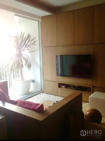 คอนโด ให้เช่าในWatthana, Bangkok - ห้องนั่งเล่นอบอุ่น ผนังทีวีบิวท์อิน โซฟาไม้ พรมขนนุ่ม และระเบียงมีต้นไม้กระถาง