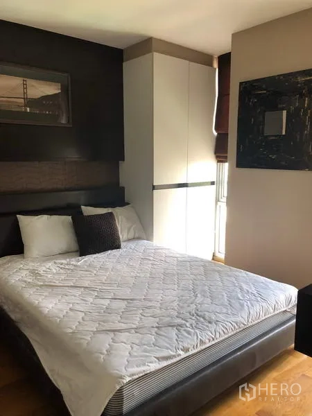 Condominium for rent in Pathum Wan, Bangkok - Cozy bedroom with queen bed, built-in wardrobe and dark feature wall by the window.