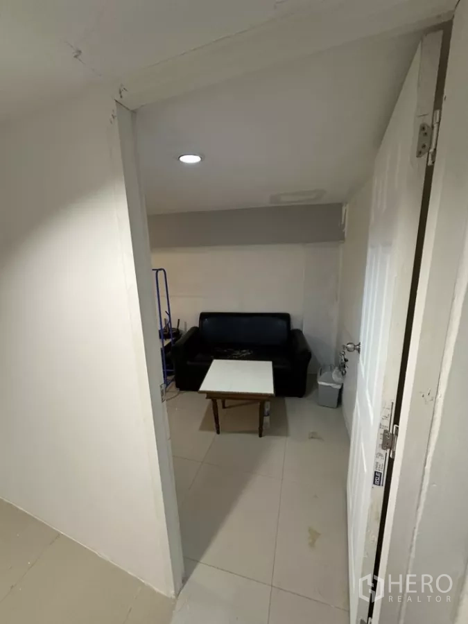 พื้นที่ขายปลีก ให้เช่า - ห้องด้านหลังขนาดกะทัดรัด มีโซฟาหนังสีดำ โต๊ะกลาง และไฟฝังฝ้า