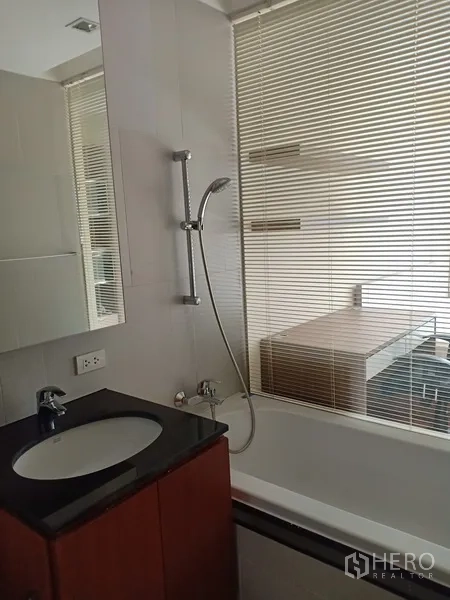 公寓 出租在Sathon, Bangkok - 现代浴室配浴缸、手持花洒与洗手台，窗设百叶帘。