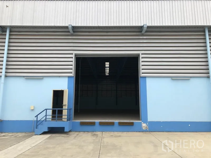 Warehouse for rent in Samut Prakan - Elevated loading dock with large roller shutter and side personnel door for access.