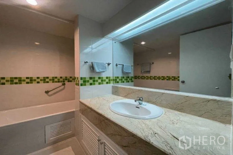 Condominium for rent in Watthana, Bangkok - Modern bathroom vanity with large mirror, bathtub and green tile border.