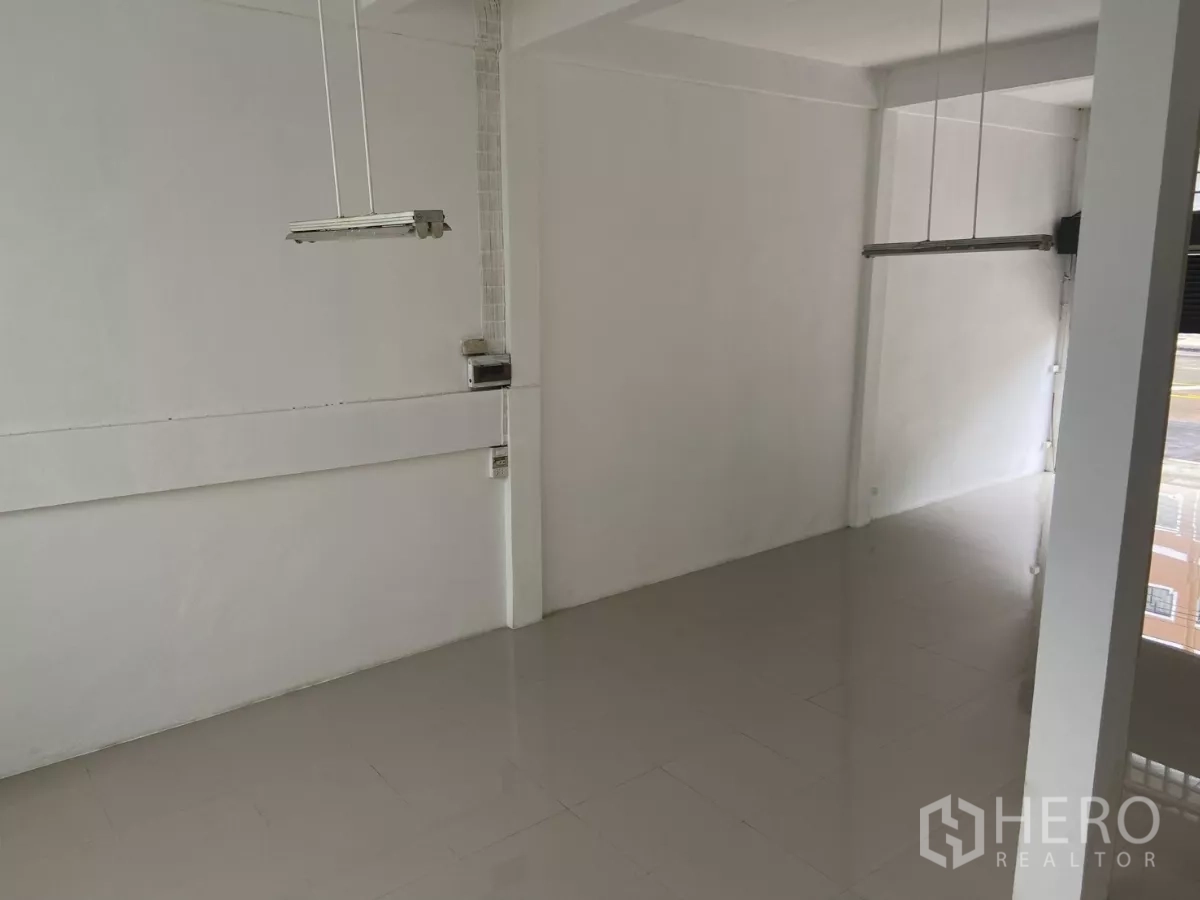 Shophouse for rent in Prawet, Bangkok - Front retail area with high ceiling, hanging lights and street-facing shutters.