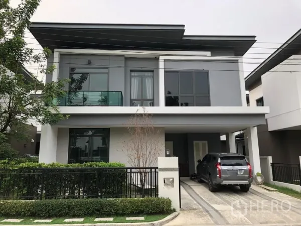 Detached House for rent in Saphan Sung, Bangkok - Modern two-storey detached house with carport, driveway and glass balcony behind a gated hedge.