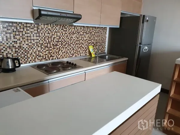 Condominium for rent in Watthana, Bangkok - Modern kitchenette with mosaic tile backsplash, electric cooktop, range hood, sink and stainless-steel refrigerator.
