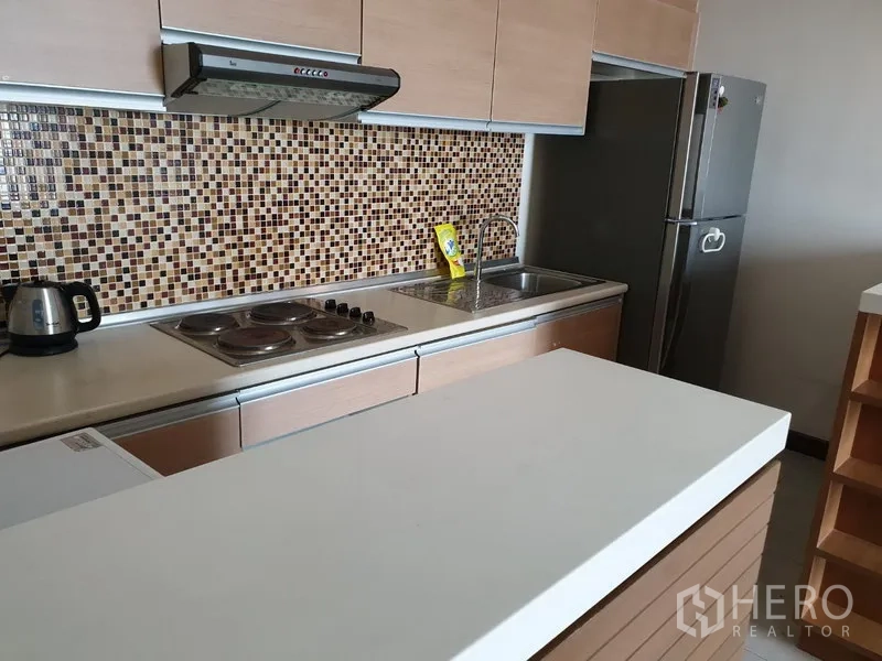 Condominium for rent in Watthana, Bangkok - Modern kitchenette with mosaic tile backsplash, electric cooktop, range hood, sink and stainless-steel refrigerator.