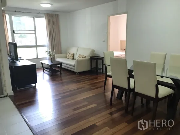 Condominium for rent in Watthana, Bangkok - Bright living and dining area with wood floors, glass table, TV stand and a large window.