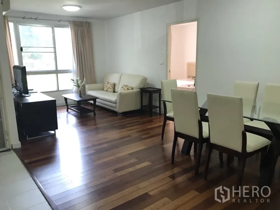 Condominium for rent in Watthana, Bangkok - Bright living and dining area with wood floors, glass table, TV stand and a large window.