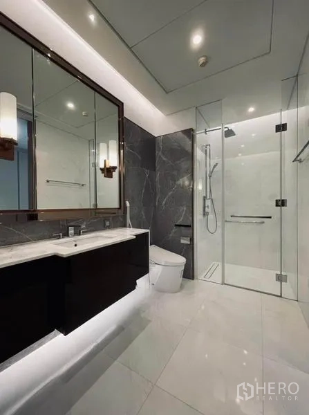 Condominium for rent in Pathum Wan, Bangkok - Contemporary bathroom featuring a glass-enclosed rain shower, floating vanity, and large mirrors.
