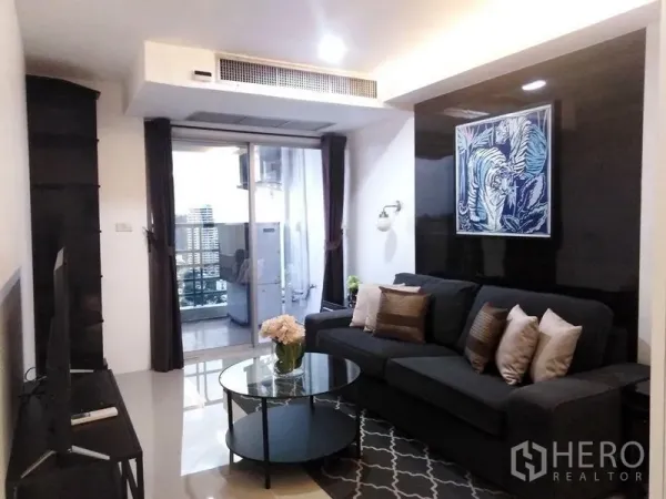 คอนโด ให้เช่าในKhlong Toei, Bangkok - ห้องนั่งเล่นอบอุ่น โซฟาสีเข้ม โต๊ะกระจก โทรทัศน์ และระเบียงมองเห็นวิวเมือง