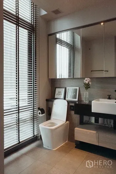 Condominium for rent in Watthana, Bangkok - Bright bathroom with large window blinds, vanity with vessel sink, and toilet.