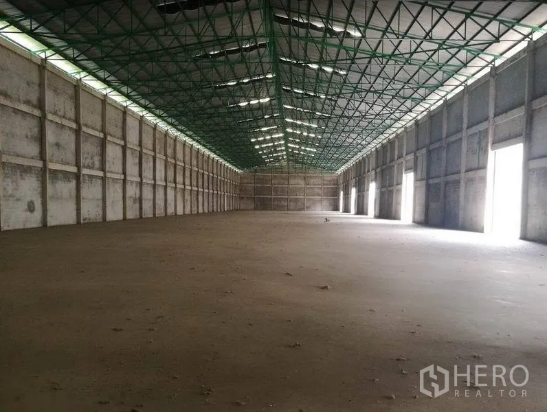 货栈 出租在Bang Sao Thong, Samut Prakan - 宽敞仓库内部，高挑钢结构屋顶带采光带，两侧多扇装卸门。