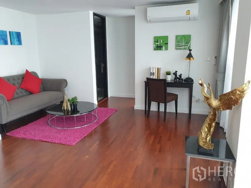 Condominium for rent in Bang Rak, Bangkok - Secondary lounge with tufted sofa, magenta rug, writing desk and decorative gold sculpture.