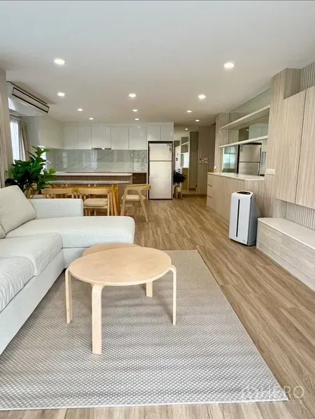 Detached House for rent in Bang Rak, Bangkok - Open-plan living room with sofa, wood floors, recessed lighting, and a bright white kitchen.