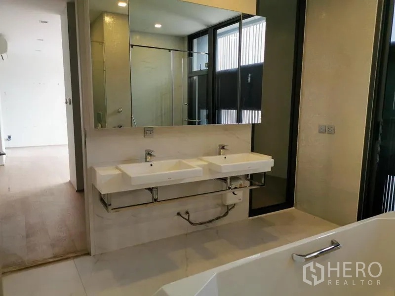 Detached House for sale in Wang Thonglang, Bangkok - Primary bathroom with double sinks, large mirror, glass shower and the edge of a bathtub.