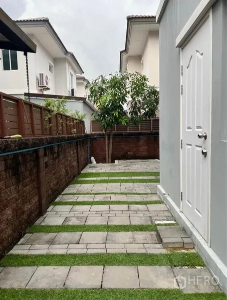 独立式住宅 出租在Suan Luang, Bangkok - 侧院铺石步道夹草缝，带外部储物间门