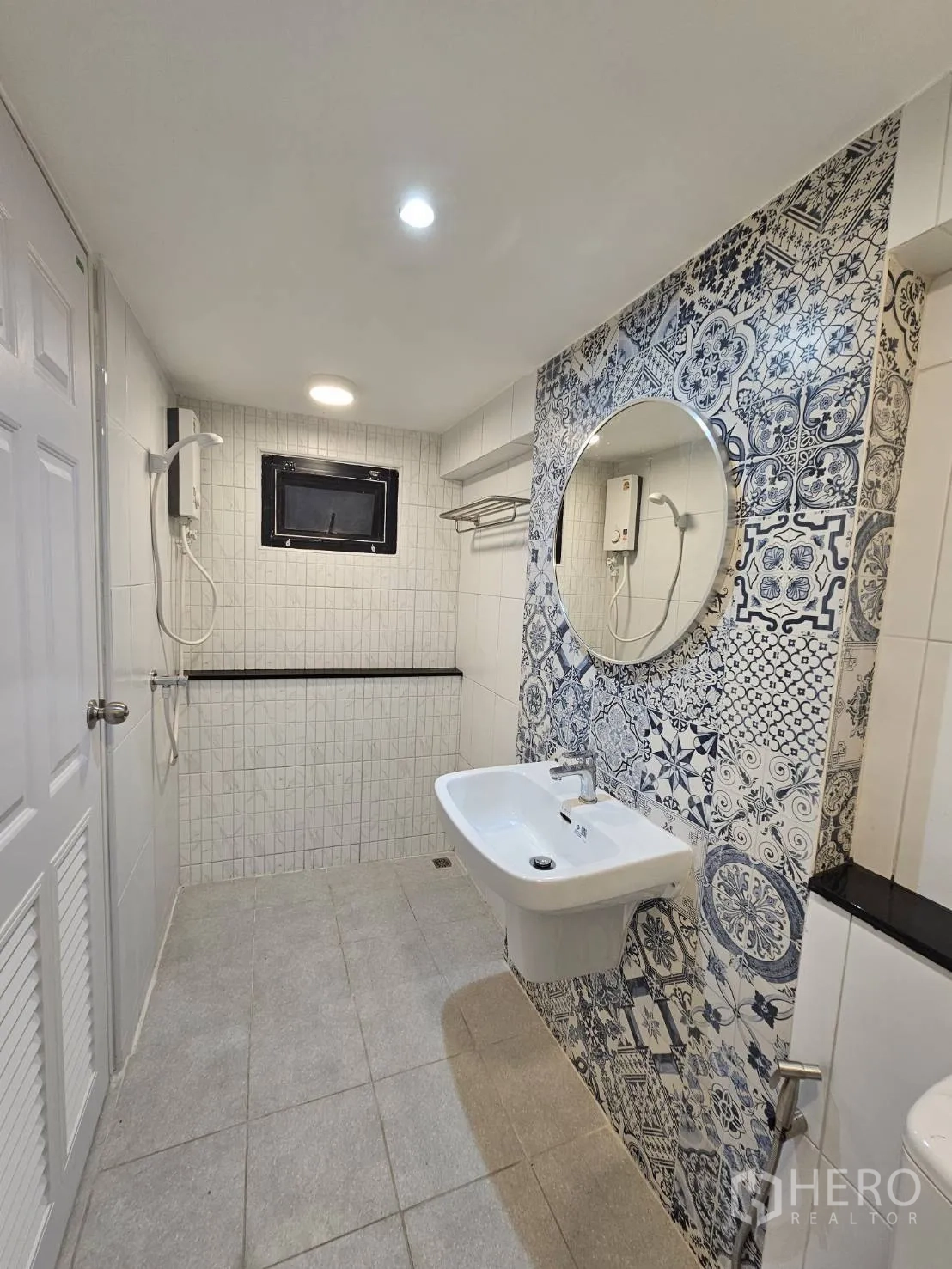 店屋 出租 - 卫生间配淋浴与热水器，白色瓷砖和圆镜。