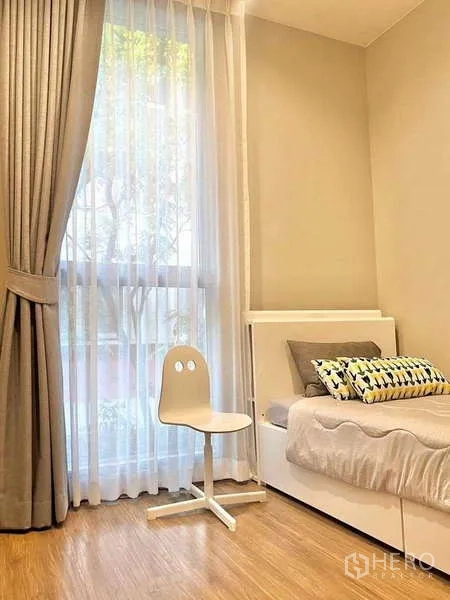 Condominium for sale in Watthana, Bangkok - Cozy second bedroom with single bed and tall window with sheer curtains.