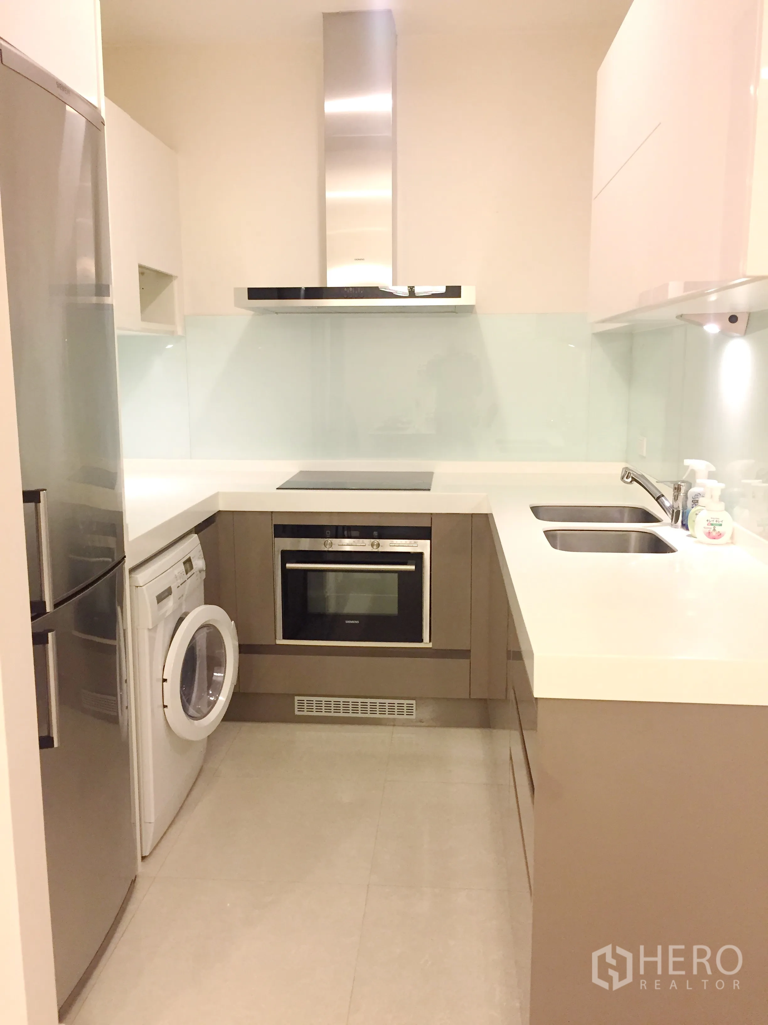Condominium for rent in Pathum Wan, Bangkok - Contemporary kitchen with oven, cooktop, fridge and washing machine under white countertops.