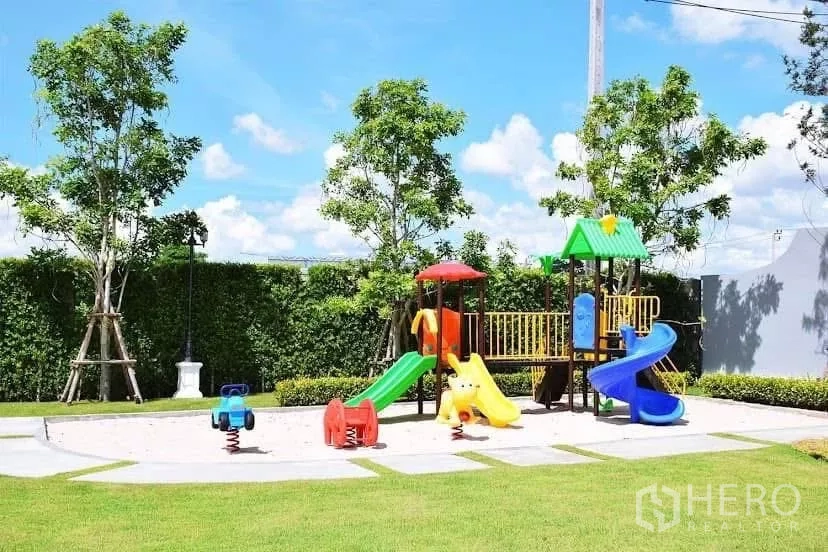 บ้าน ให้เช่าในPrawet, Bangkok - สนามเด็กเล่นส่วนกลางพร้อมเครื่องเล่นสีสันสดใส รายล้อมด้วยสนามหญ้าและต้นไม้.