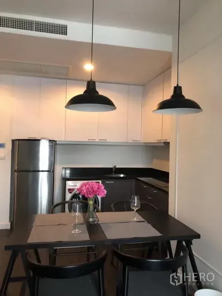 คอนโด ให้เช่าในPathum Wan, Bangkok - ครัวบิวท์อินตู้สีขาว ท็อปสีดำ ตู้เย็นสแตนเลส และโต๊ะทานอาหารพร้อมโคมแขวน