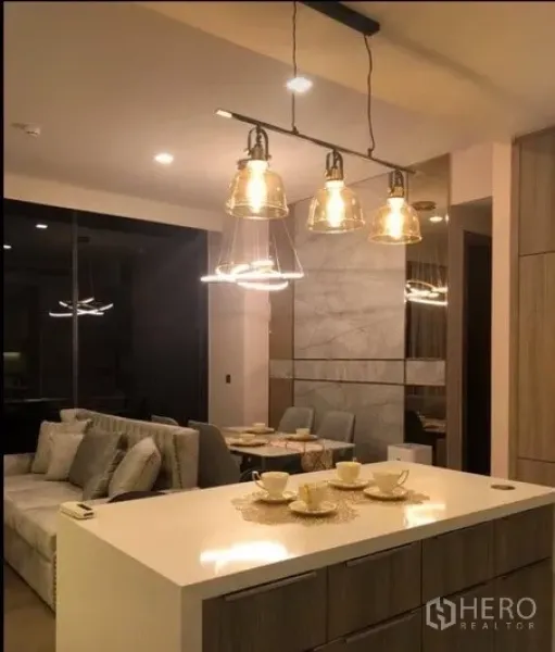 Condominium for rent in Watthana, Bangkok - Warm-lit open-plan kitchen with an island, glass pendant lights, and a view to the dining and living areas.