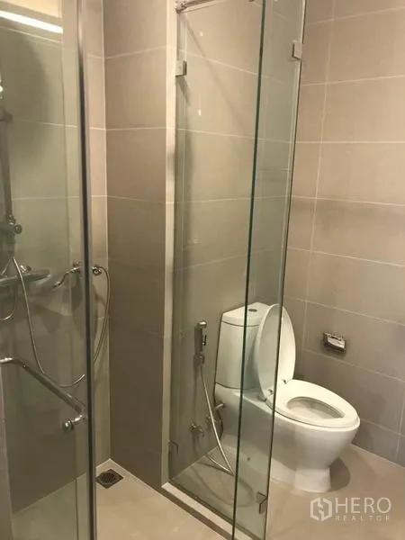 Condominium for rent or sale in Pathum Wan, Bangkok - Contemporary bathroom with glass shower stall and toilet finished in gray tiles.