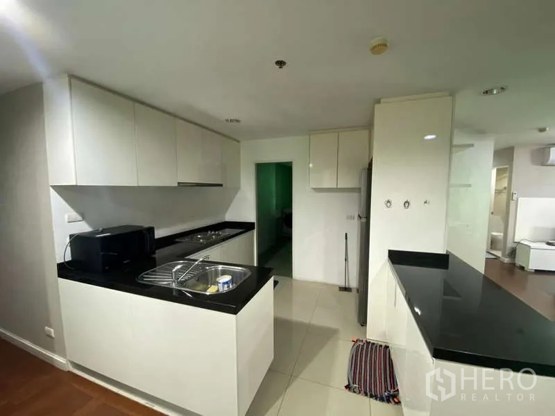Condominium for  in Huai Khwang, Bangkok - U‑shaped white kitchen with black stone countertops, sink, cooktop and refrigerator.