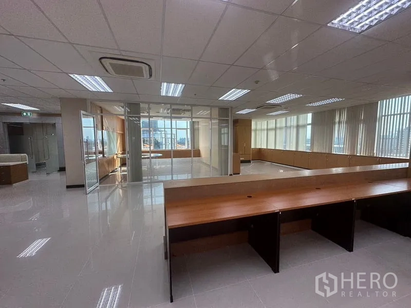Office Space for rent in Suan Luang, Bangkok - Spacious office floor with benching desks facing a glass-walled executive room and full-height windows.