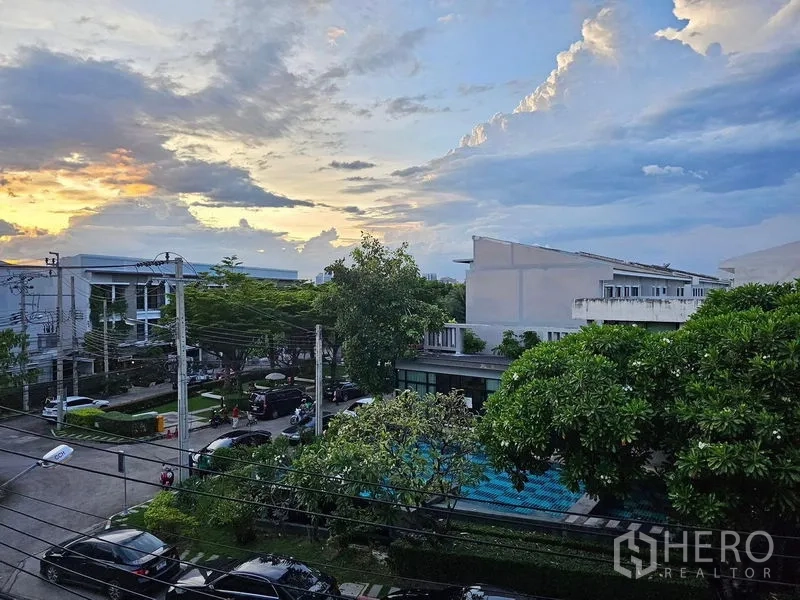 Townhouse for rent in Wang Thonglang, Bangkok - Balcony view over a leafy residential community with pool and parking at sunset.