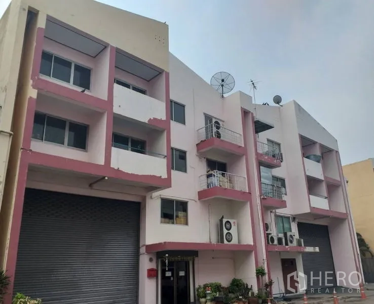 โรงงาน ขายในKhlong Luang, Pathum Thani - อาคารโรงงานสีชมพูขาวด้านหน้า มีประตูม้วนและระเบียง.