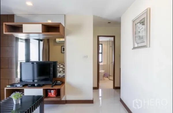 房间 出租在Bang Rak, Bangkok - 从客厅望向浴室的走廊视角，可见电视柜与置物架。