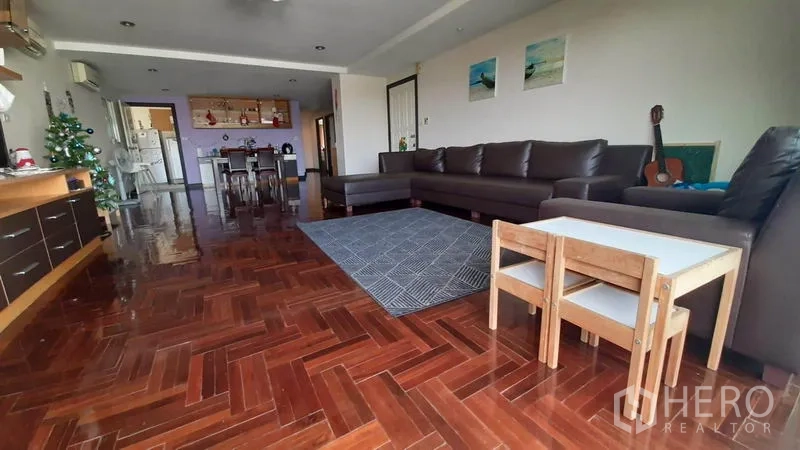 คอนโด ให้เช่าในWatthana, Bangkok - ห้องนั่งเล่นขนาดใหญ่ โซฟาหนังรูปตัวแอล พรม และพื้นปาร์เกต์ลายก้างปลา เชื่อมส่วนทานอาหารและครัว